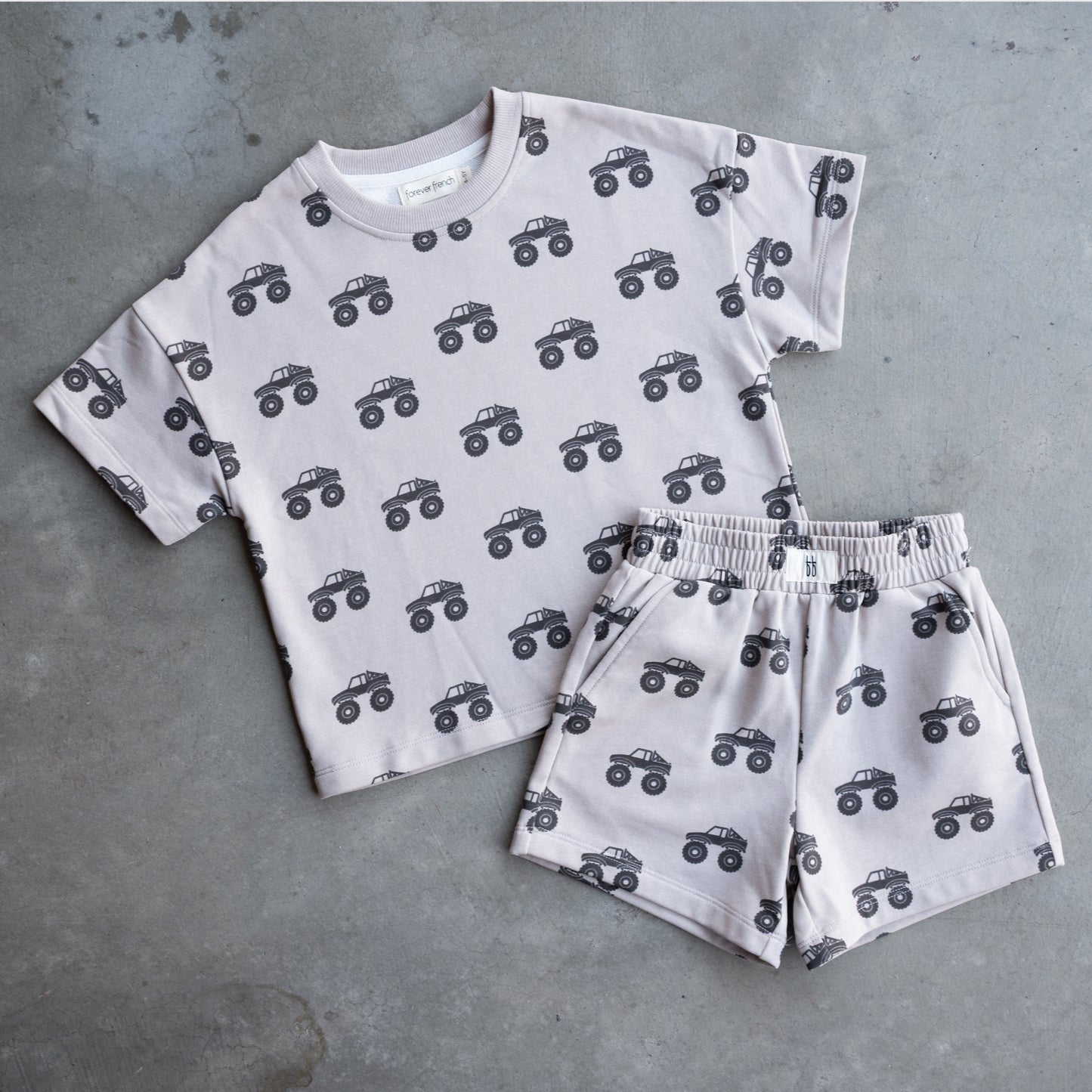 The forever french baby French Terry Short Set | Monster Truck features a light gray short sleeve top and shorts with a black monster truck pattern, displayed on a gray surface.