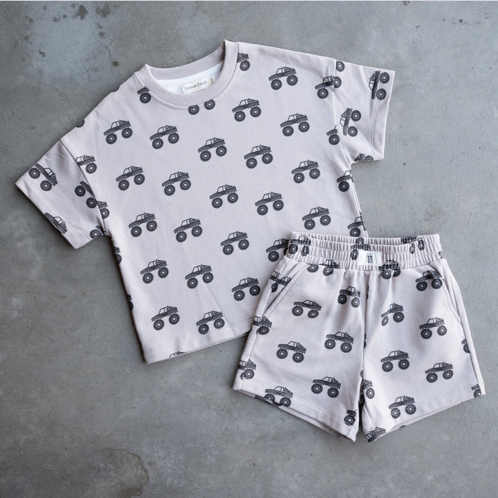 The forever french baby French Terry Short Set | Monster Truck features a light gray short sleeve top and shorts with a black monster truck pattern, displayed on a gray surface.