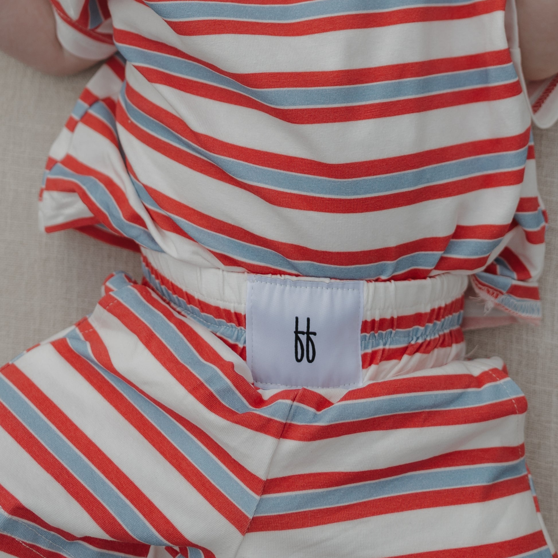 A child in the forever french baby Child Short Set | Heritage Stripe, featuring red and blue diagonal stripes and an elastic waistband—a perfect pick for comfortable, stylish kids striped clothing.
