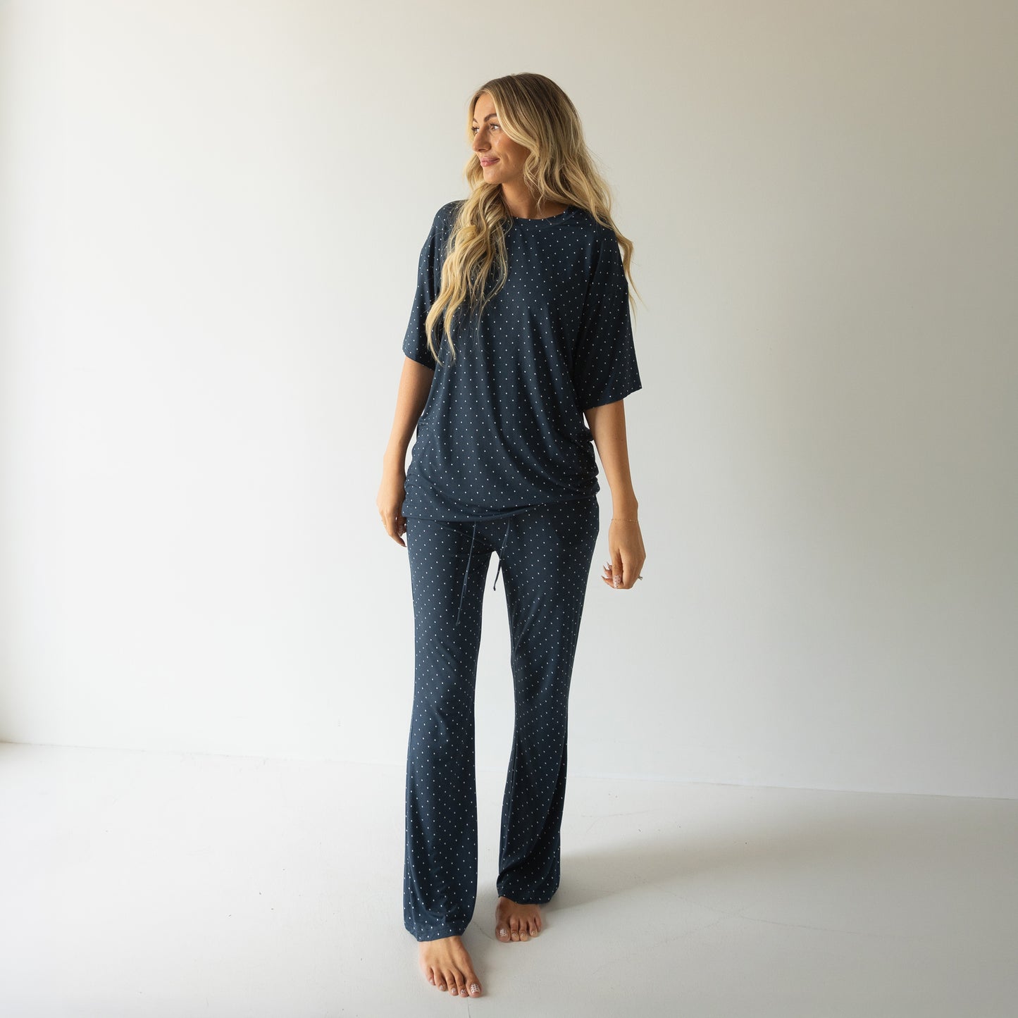 A woman with long blonde hair smiles barefoot in a minimalist room, wearing the forever french baby Short Sleeve Women's Bamboo Lounge Set | Emery—a cozy, stylish pick for lounging.