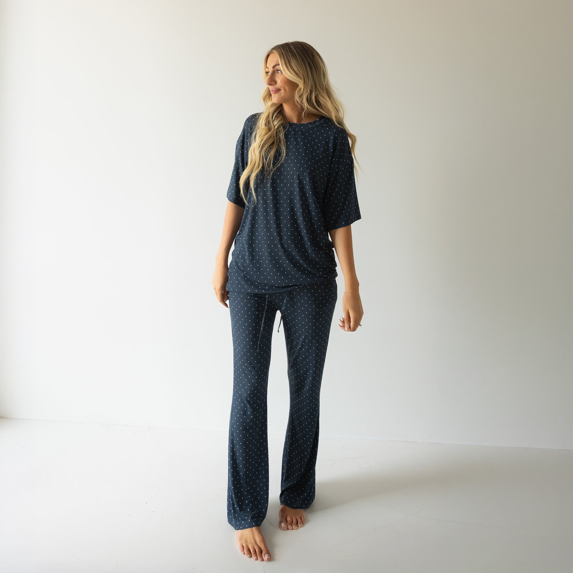 A woman with long blonde hair smiles barefoot in a minimalist room, wearing the forever french baby Short Sleeve Women's Bamboo Lounge Set | Emery—a cozy, stylish pick for lounging.