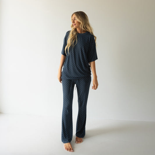 A woman with long blonde hair smiles barefoot in a minimalist room, wearing the forever french baby Short Sleeve Women's Bamboo Lounge Set | Emery—a cozy, stylish pick for lounging.