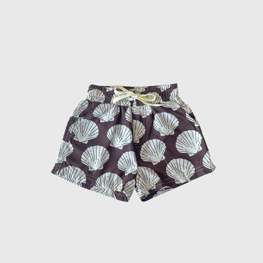 The forever french baby Child Board Short | Seashells features an elastic waistband, drawstring, and a bold seashell print on dark fabric—perfect for summer, shown on a plain light grey surface.