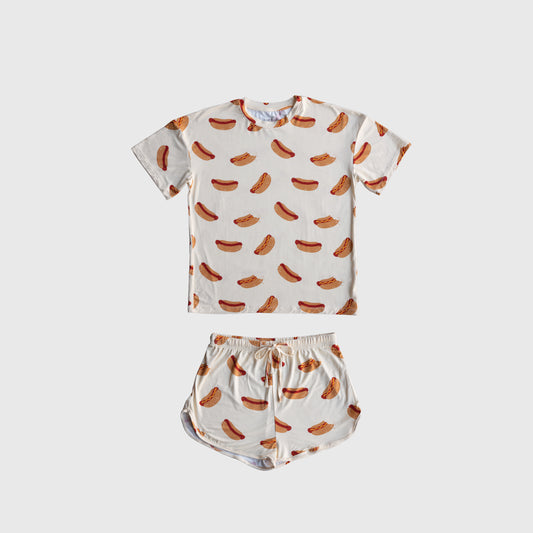 The Girl's Bamboo Short Set | Hot Dogs from forever french baby features a breathable bamboo short-sleeve tee and drawstring shorts with an all-over hot dog print on white, displayed flat against a plain surface.