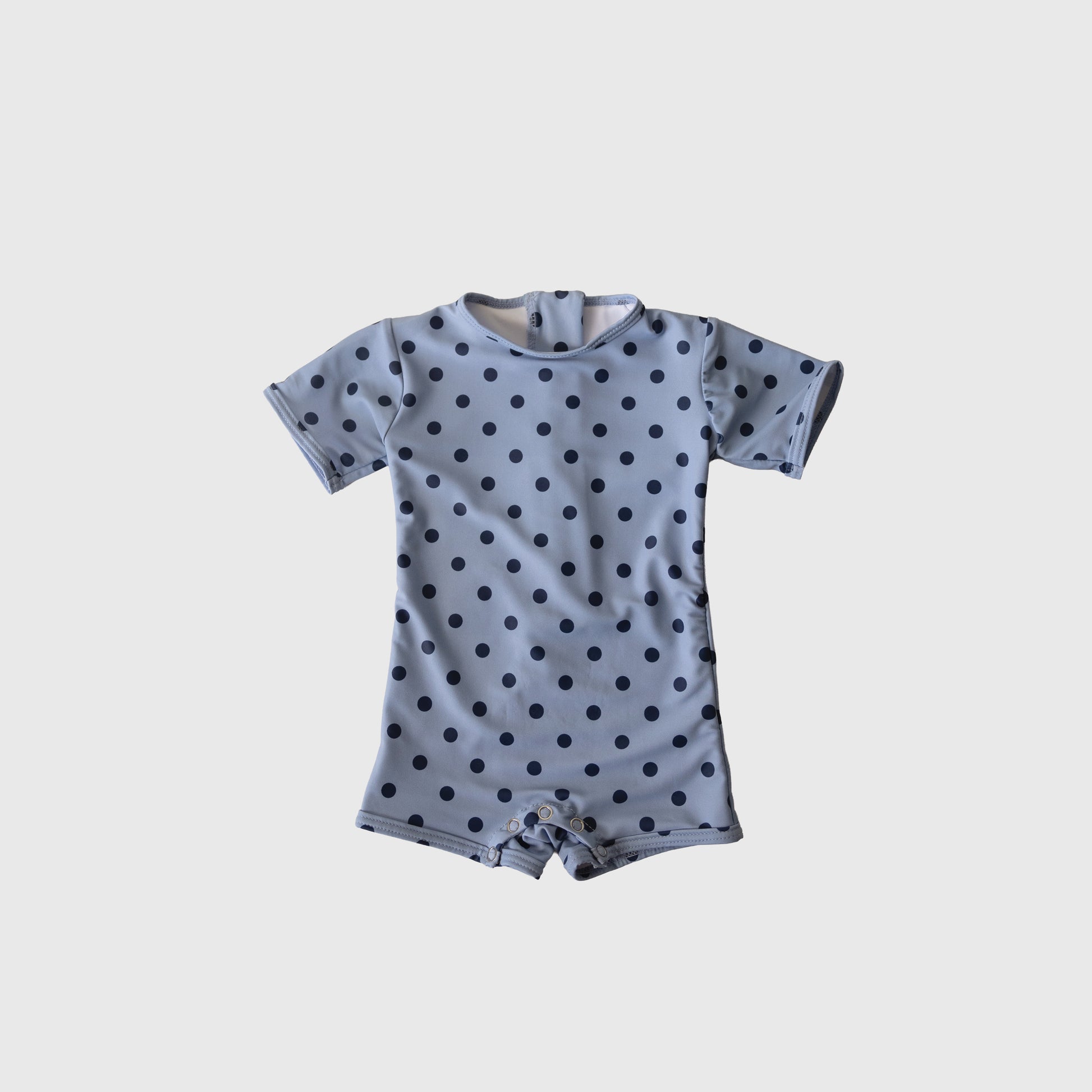 The Child Shortie Swimsuit | Sully by forever french baby is a light blue, short-sleeve romper with black polka dots and a round neck, displayed flat on a white background—ideal for your little one's first swim or playful days.