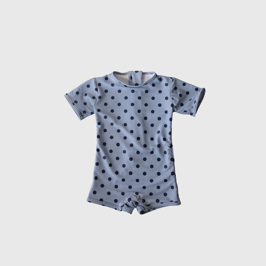 The Child Shortie Swimsuit | Sully by forever french baby is a light blue, short-sleeve romper with black polka dots and a round neck, displayed flat on a white background—ideal for your little one's first swim or playful days.