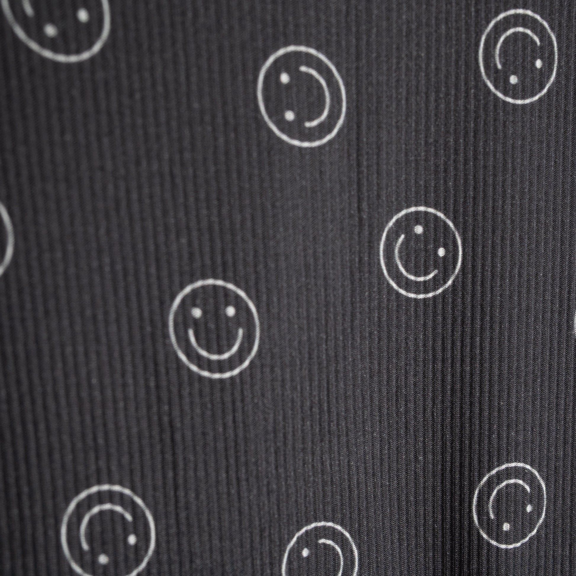 A close-up of the forever french baby Child Boxy Tee Lounge Set | Smiley Ribbed shows dark ribbed fabric with white outlined smiley faces, some full and some partial—perfectly spaced and ideal for comfy, breathable children's loungewear.