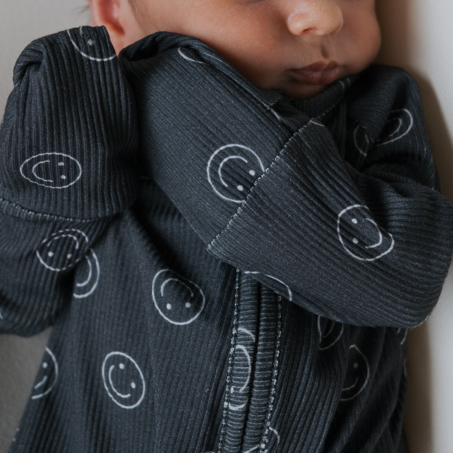 Close-up of a baby in forever french baby Bamboo Zip Pajamas | Smiley Ribbed, featuring white smiley face patterns. These soft, hypo-allergenic pajamas are gentle on sensitive skin and provide all-night comfort.
