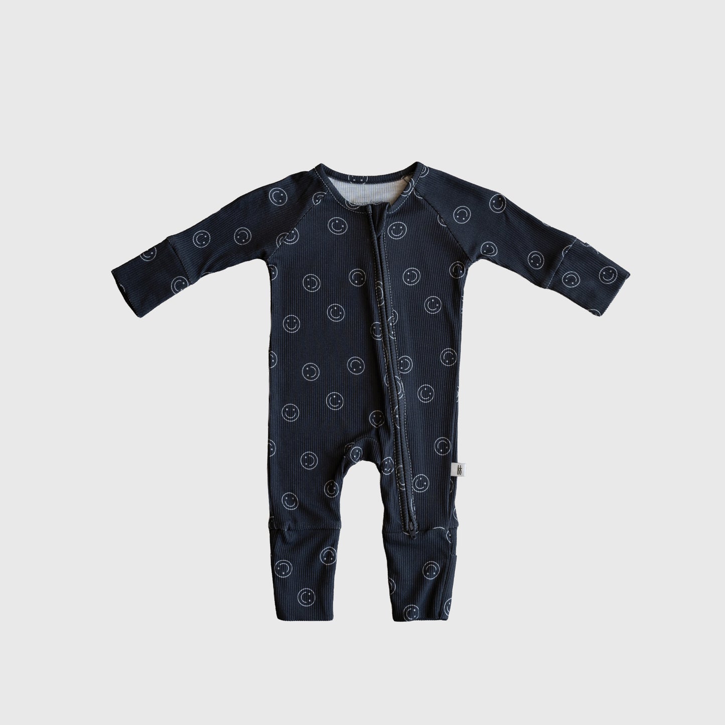 The forever french baby Bamboo Zip Pajamas | Smiley Ribbed feature dark blue ribbed bamboo fabric, a white smiley face print, long sleeves, and a diagonal neck-to-leg zipper, shown on a light gray background.