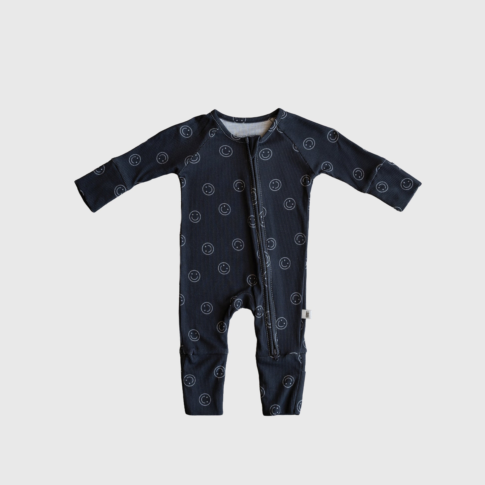 The forever french baby Bamboo Zip Pajamas | Smiley Ribbed feature dark blue ribbed bamboo fabric, a white smiley face print, long sleeves, and a diagonal neck-to-leg zipper, shown on a light gray background.