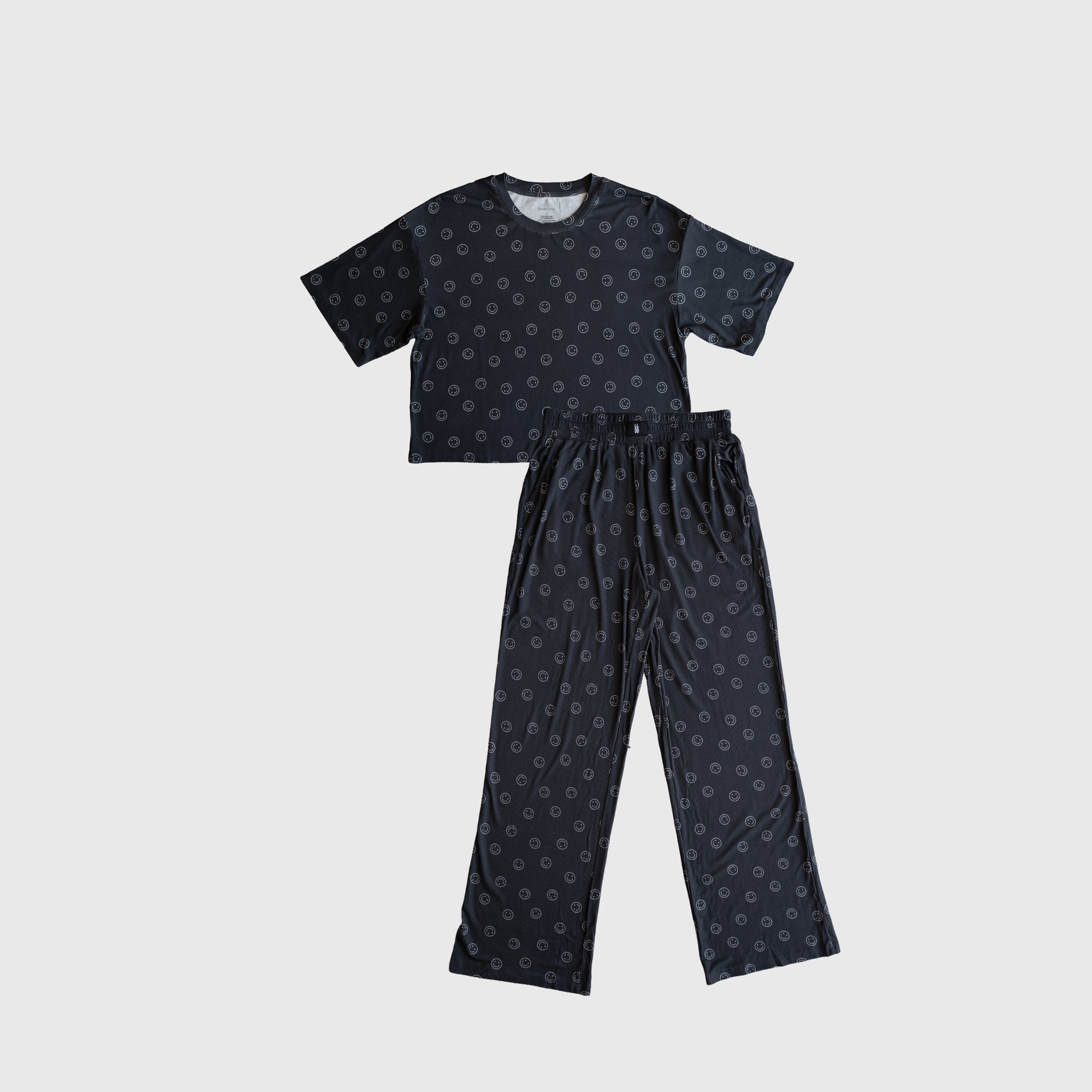 The forever french baby Women's Boxy Tee Lounge Set | Smiley Ribbed is a two-piece hypo-allergenic bamboo set with a short-sleeve black top and matching long pants, both featuring a subtle circular pattern, shown on a white background.