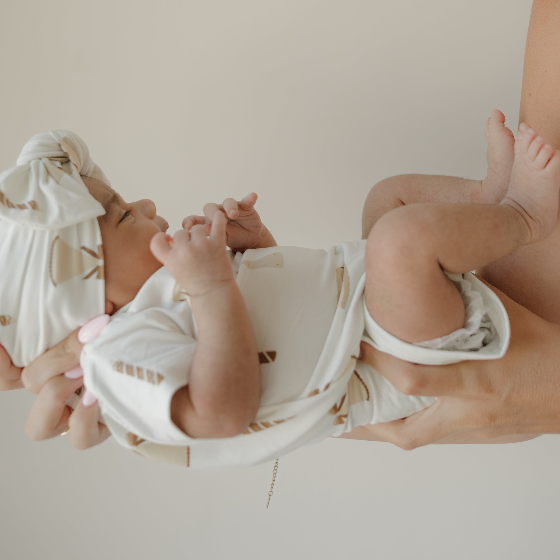 A newborn dressed in the forever french baby Short Sleeve Bamboo Snapsuit | Birthday Girl is gently cradled in an adult’s arms against a light background, ensuring both comfort and peace of mind.