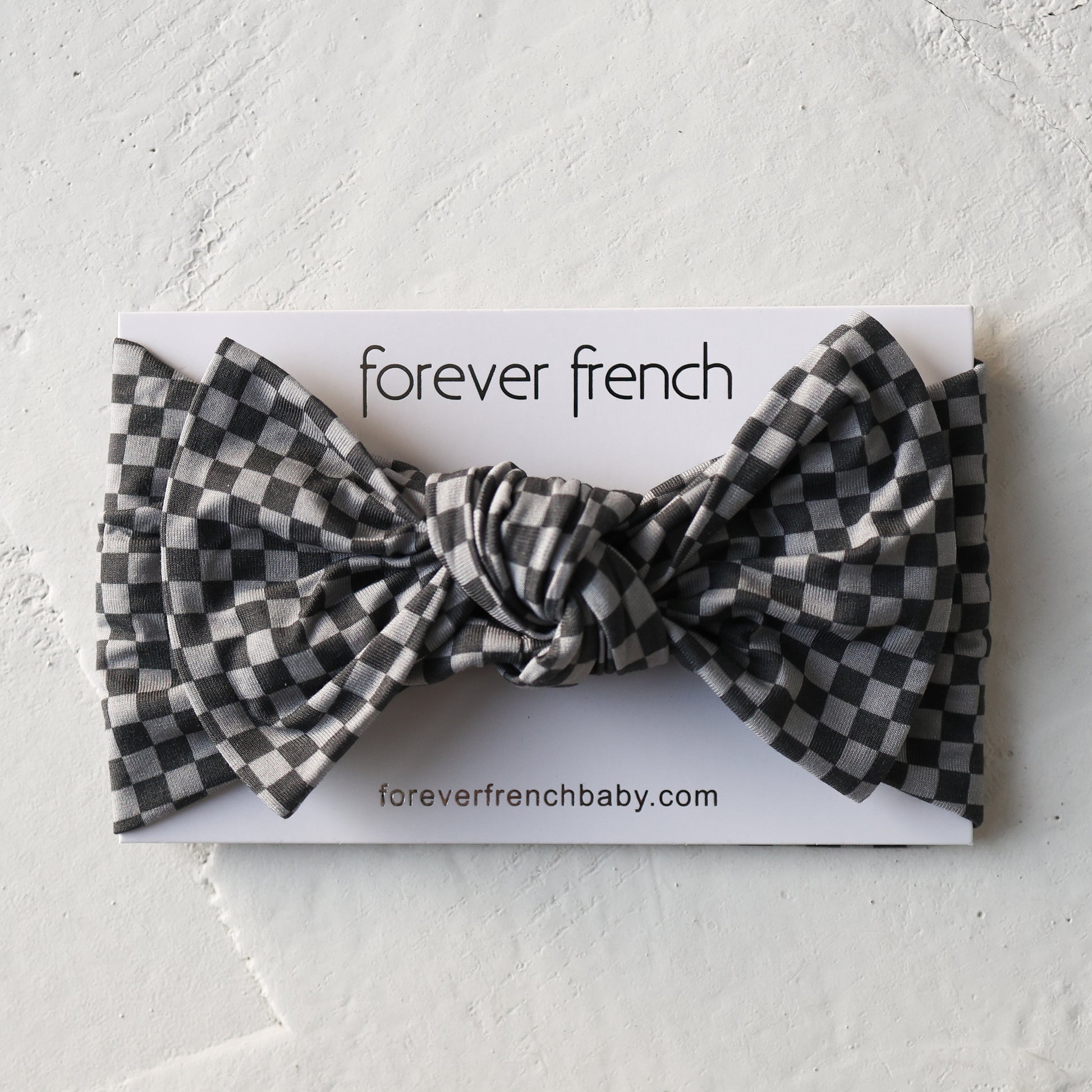 The Bamboo Head Wrap | Street Micro Check by forever french baby is shown on a branded card with "foreverfrenchbaby.com" against a textured white background. The headband features a black and white checkered pattern.