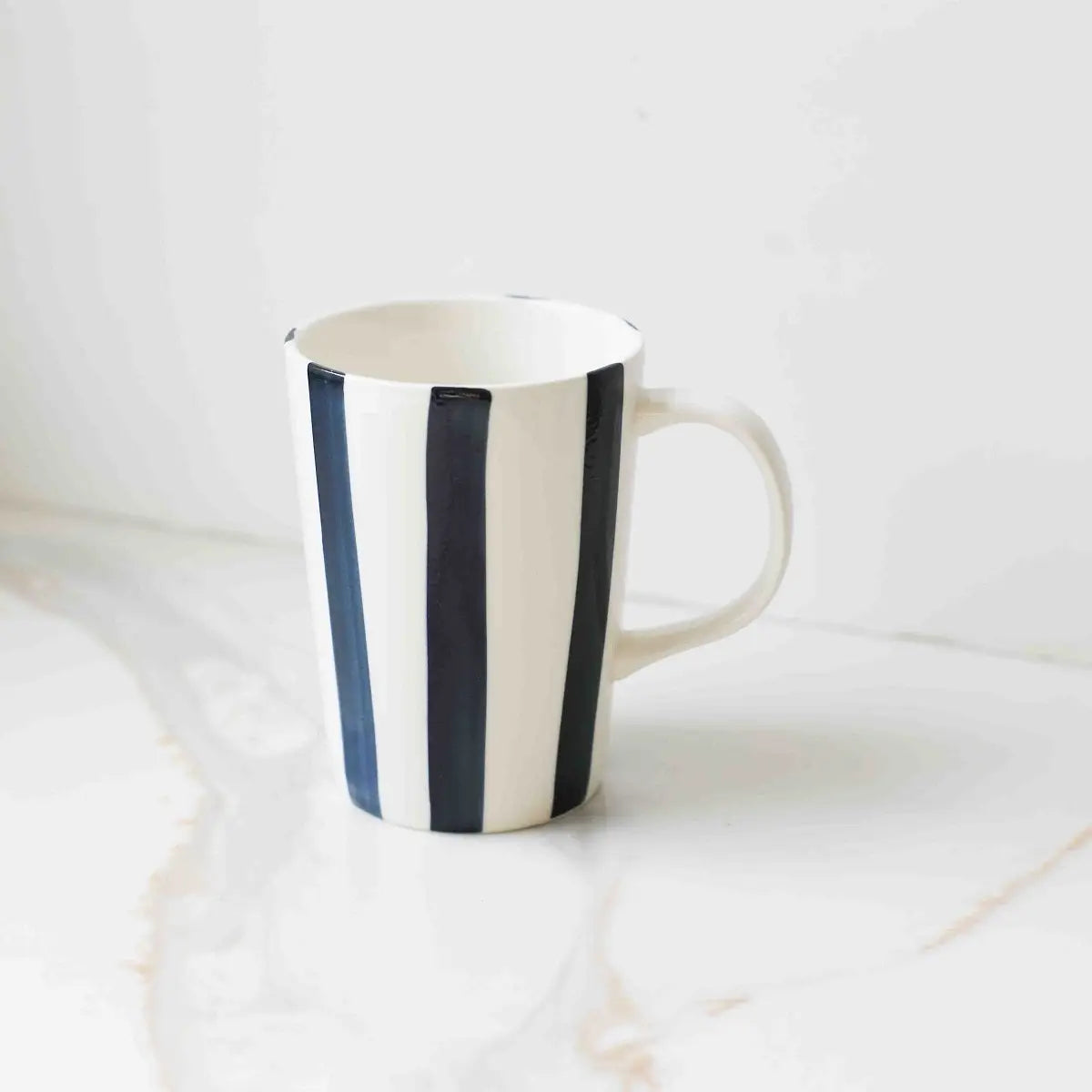The Fodory Hand-Painted Striped Ceramic Cup, featuring bold vertical black stripes, sits on a white marble surface.