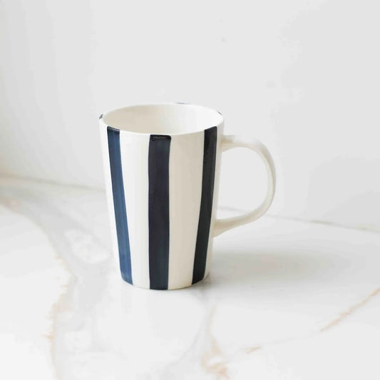 The Fodory Hand-Painted Striped Ceramic Cup, featuring bold vertical black stripes, sits on a white marble surface.