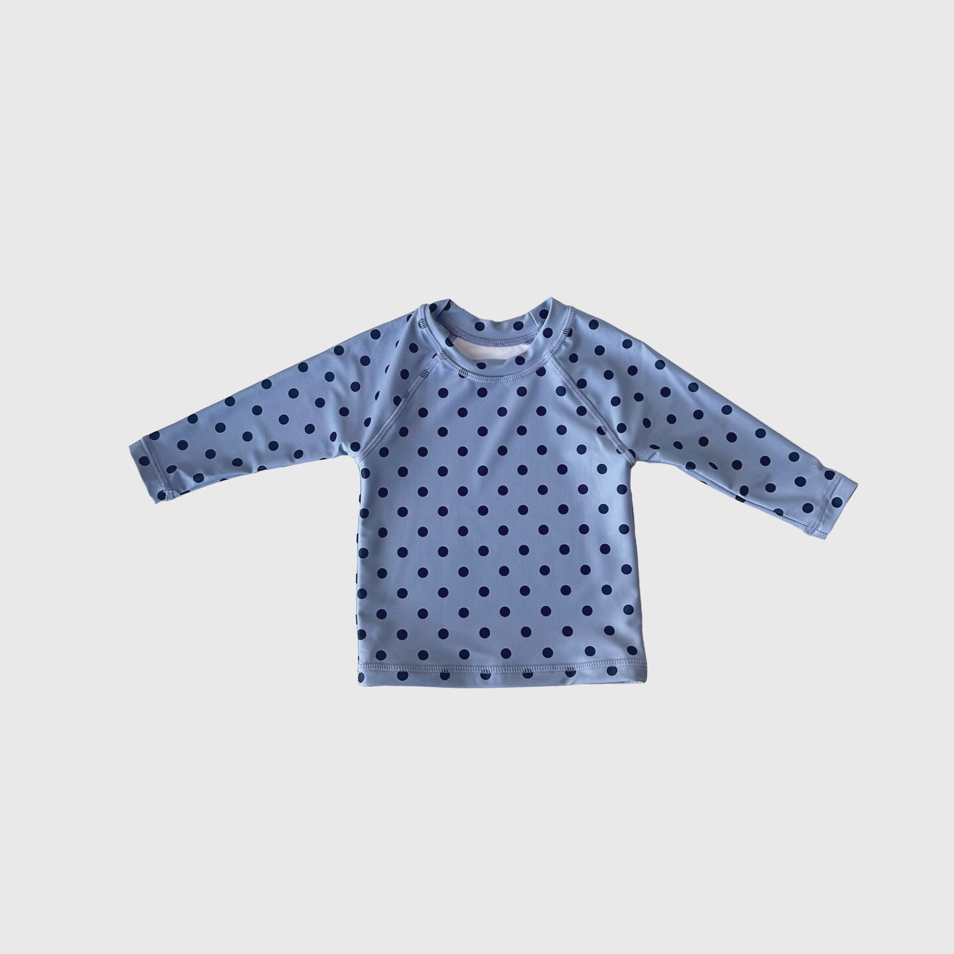 The Child Rash Guard | Sully by forever french baby is a light blue, long-sleeve kids’ swim top with dark blue polka dots for stylish sun protection, shown against a plain white background.