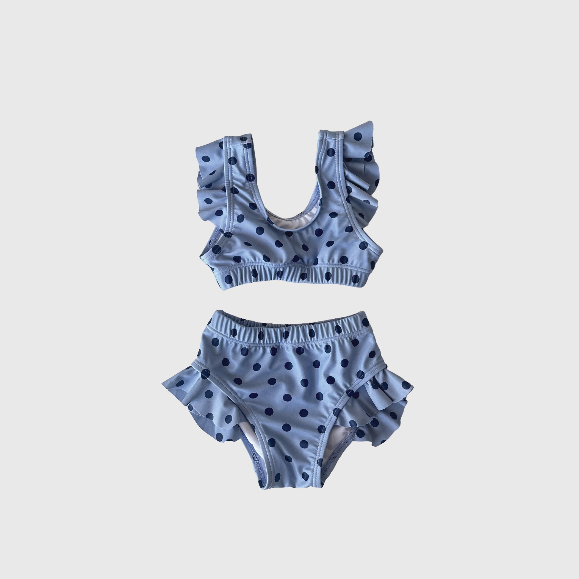 The Girl's Two Piece Swimsuit | Sully by forever french baby is a charming light blue set with playful blue polka dots and ruffled straps and hips, shown on a white background.