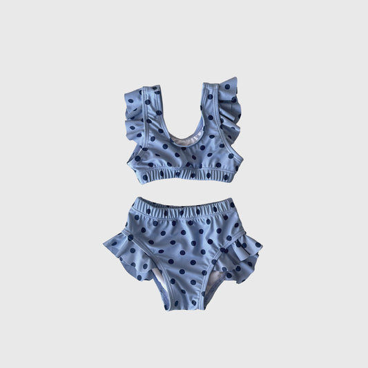 The Girl's Two Piece Swimsuit | Sully by forever french baby is a charming light blue set with playful blue polka dots and ruffled straps and hips, shown on a white background.