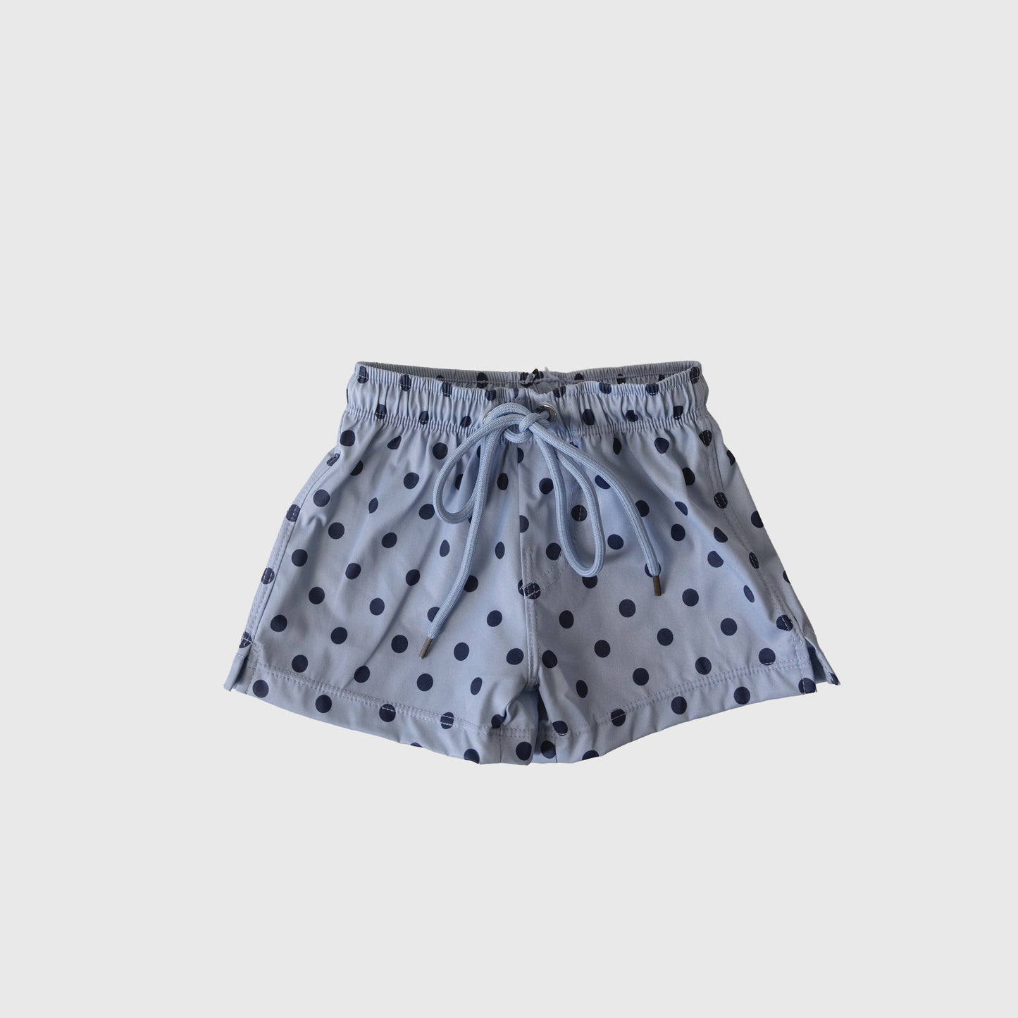 The forever french baby Child Board Short | Sully features light blue fabric with navy polka dots, an elastic waistband, and blue drawstring. Perfect for coordinated family looks, these kids’ swim shorts are shown on a plain white background.