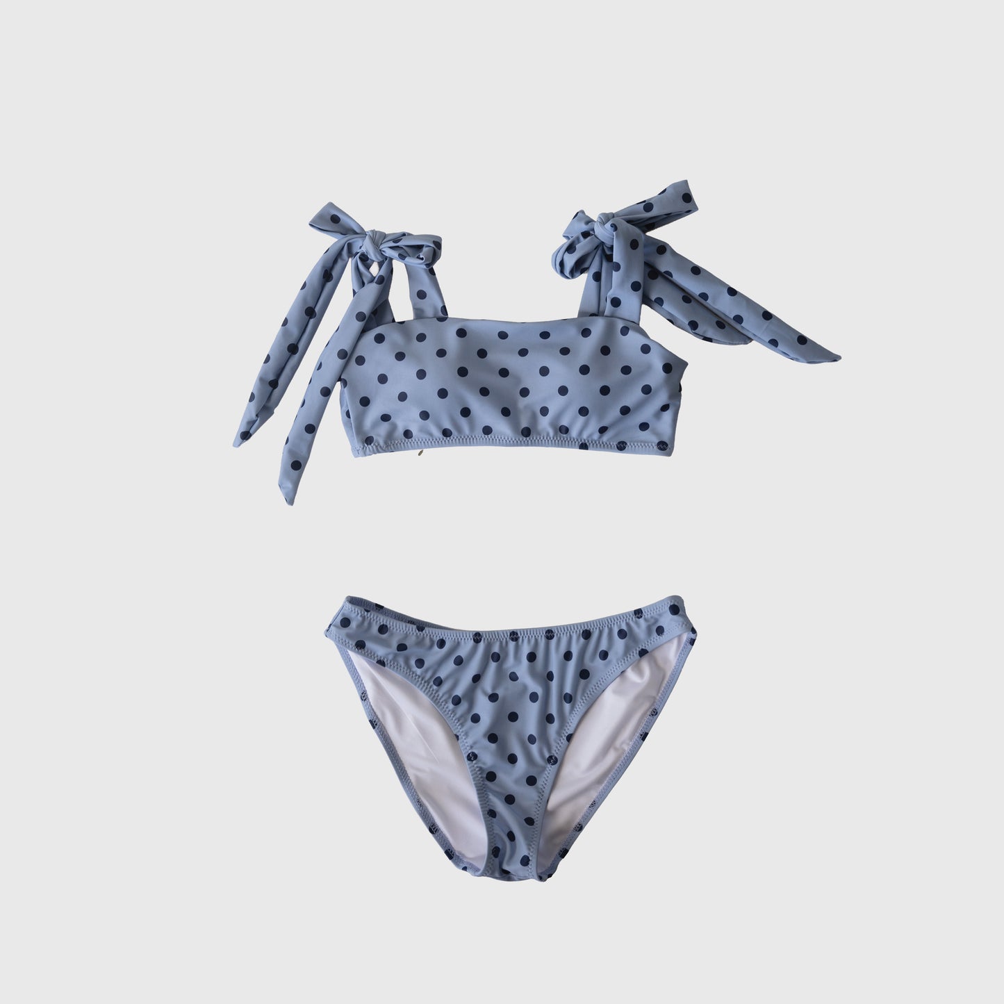 The Women's Two Piece Swimsuit | Sully by forever french baby features light blue fabric with black polka dots and shoulder tie straps, shown on a plain white background.