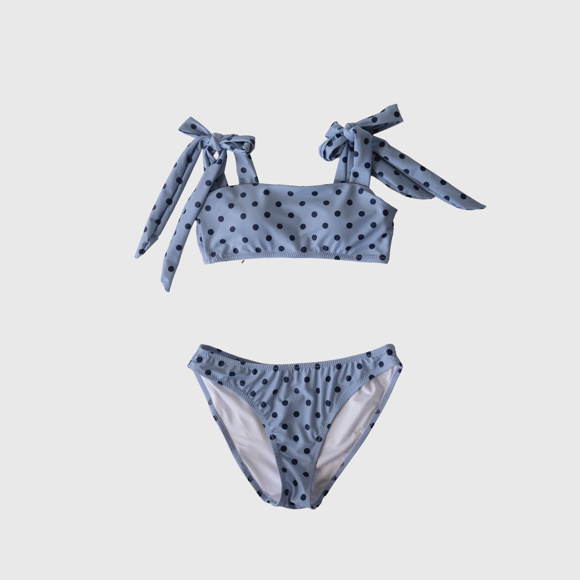 The Women's Two Piece Swimsuit | Sully by forever french baby features light blue fabric with black polka dots and shoulder tie straps, shown on a plain white background.