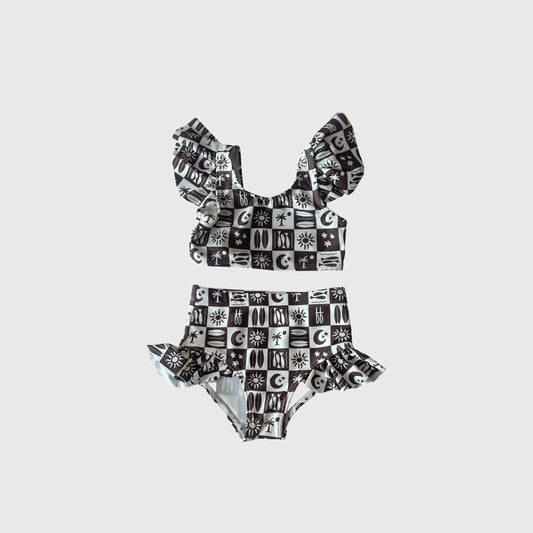 The Girl's Two Piece Swimsuit | Summer Check by forever french baby features ruffled straps and waist with suns, moons, eyes, and celestial symbols on a black and white checkered design—a stylish pick in kids swimwear.