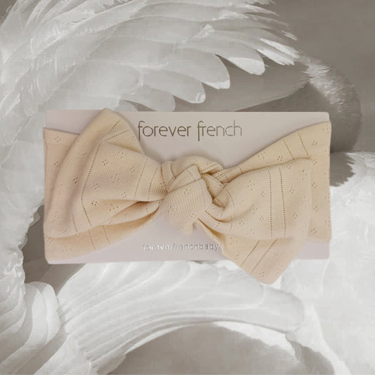 A cream-colored Pointelle Head Wrap in the shade “Swan” by forever french baby rests on a branded card, displayed atop a feathery white background. Crafted from soft pointelle cotton, this adjustable headband offers a comfortable and stylish accessory for your little one.