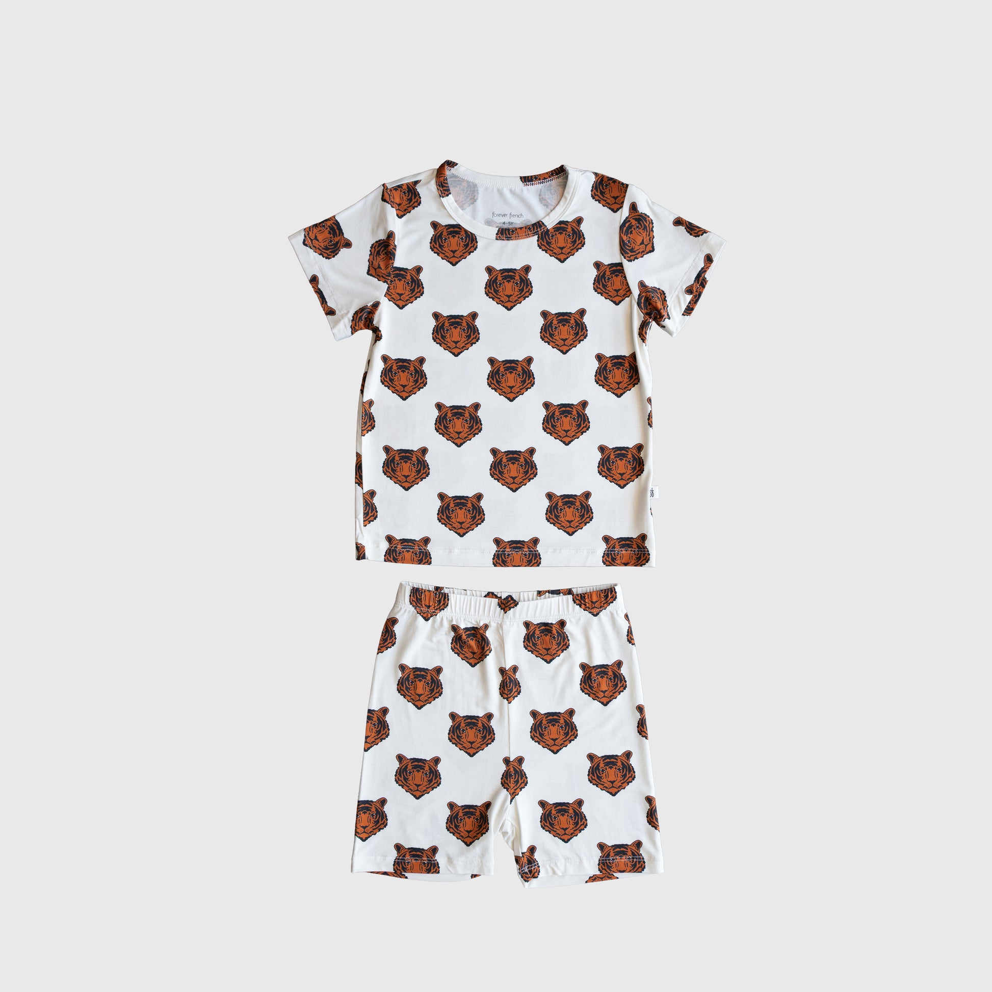 The forever french baby Bamboo Short Set | Tigers features a white short-sleeve top and shorts with an all-over brown and black tiger face print, made from breathable bamboo for comfortable, hypoallergenic kids' wear.