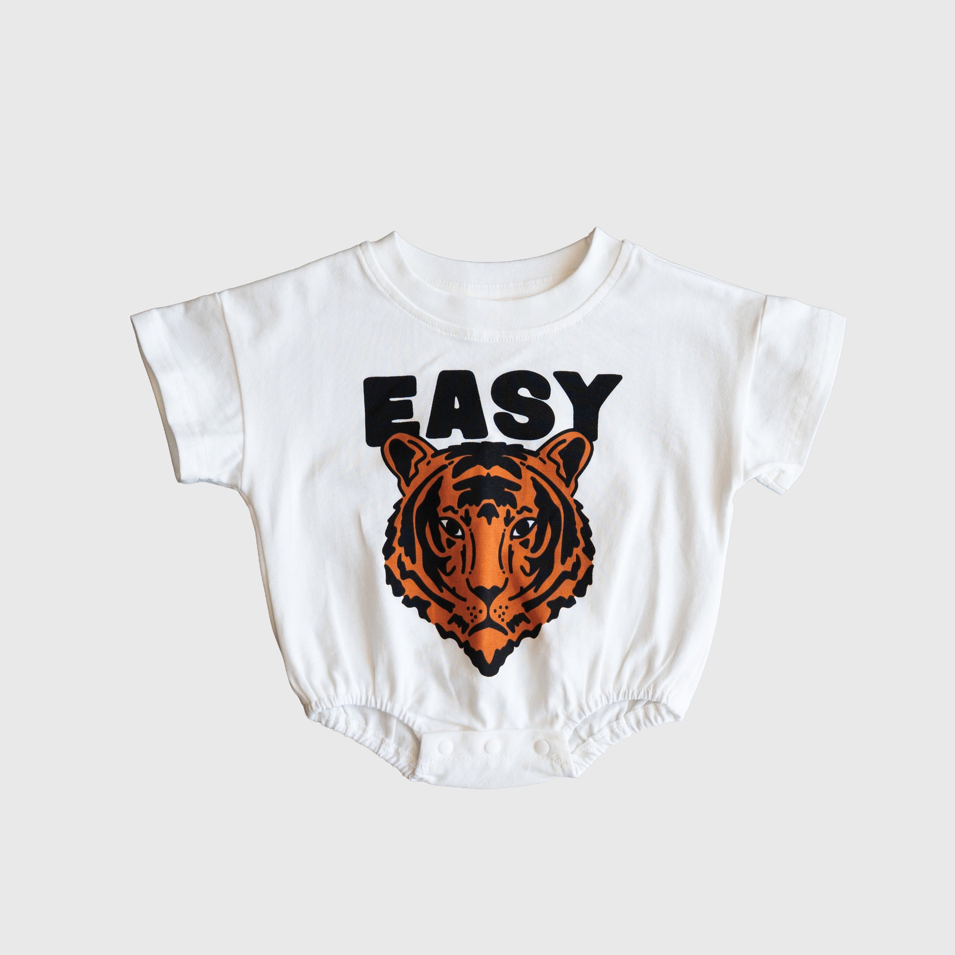 The forever french baby Short Sleeve Romper | Easy Tiger features "EASY" in bold black letters above an orange and black tiger face. Made from a comfy cotton blend, it's perfect for your little one’s everyday adventures.