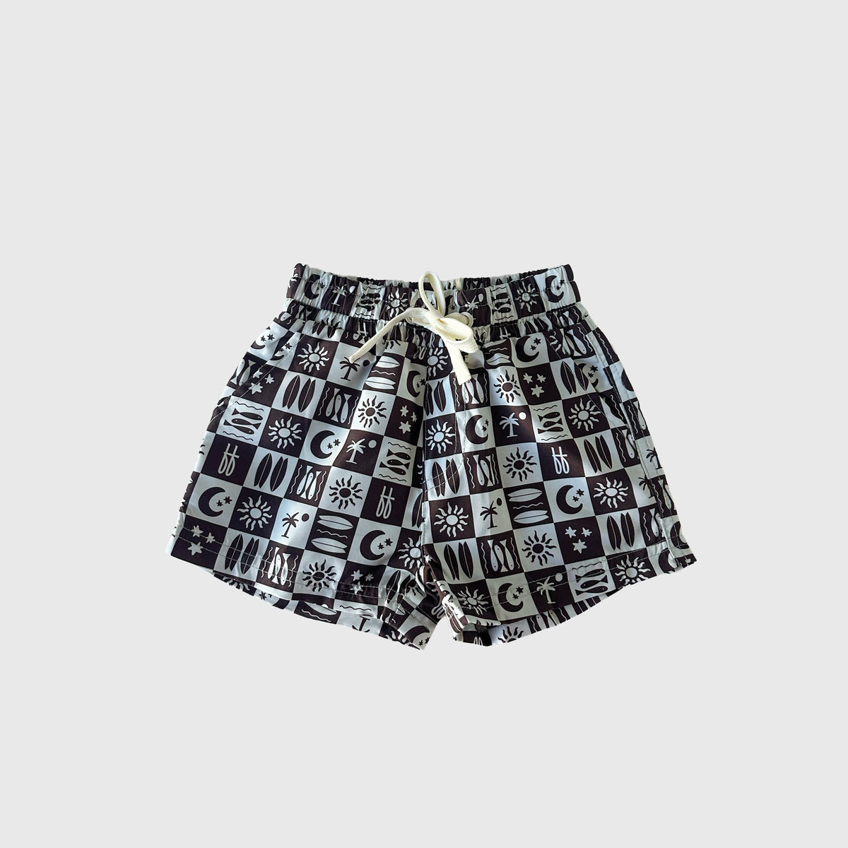 The Child Board Short | Summer Check by forever french baby is ideal for summer, featuring a black and white checkered pattern with suns, moons, surfboards, stars, plus an elastic waistband and white drawstring for comfort.