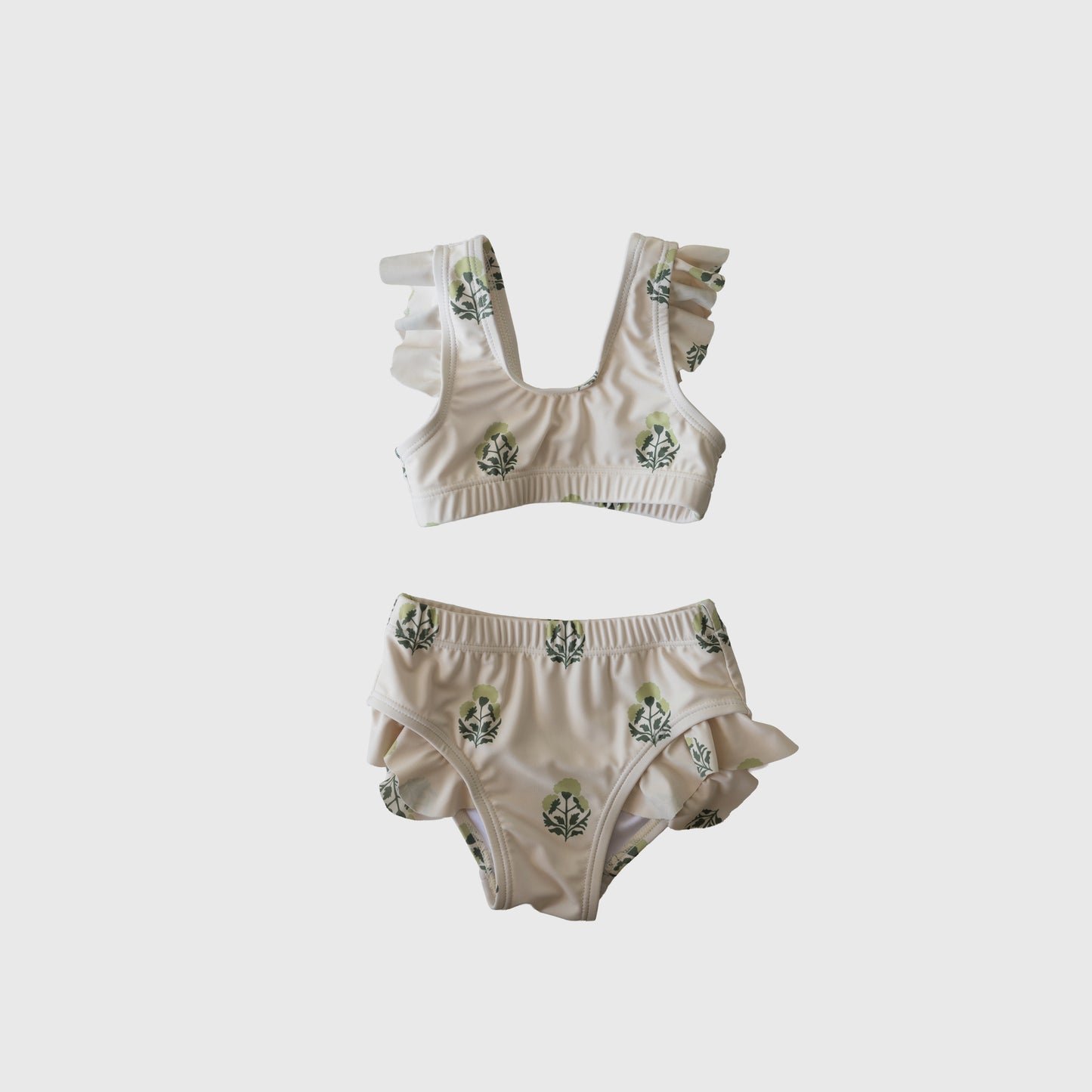 The forever french baby Girl's Two Piece Swimsuit | Marigold features ruffled straps and leg openings, a white base with green leafy print, and is displayed on a plain light gray background.