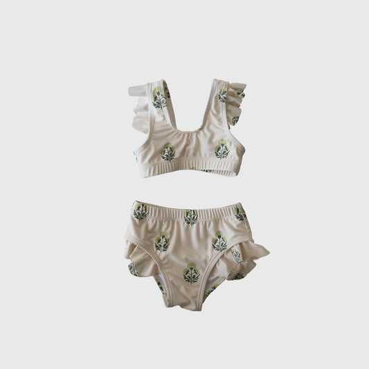 The forever french baby Girl's Two Piece Swimsuit | Marigold features ruffled straps and leg openings, a white base with green leafy print, and is displayed on a plain light gray background.