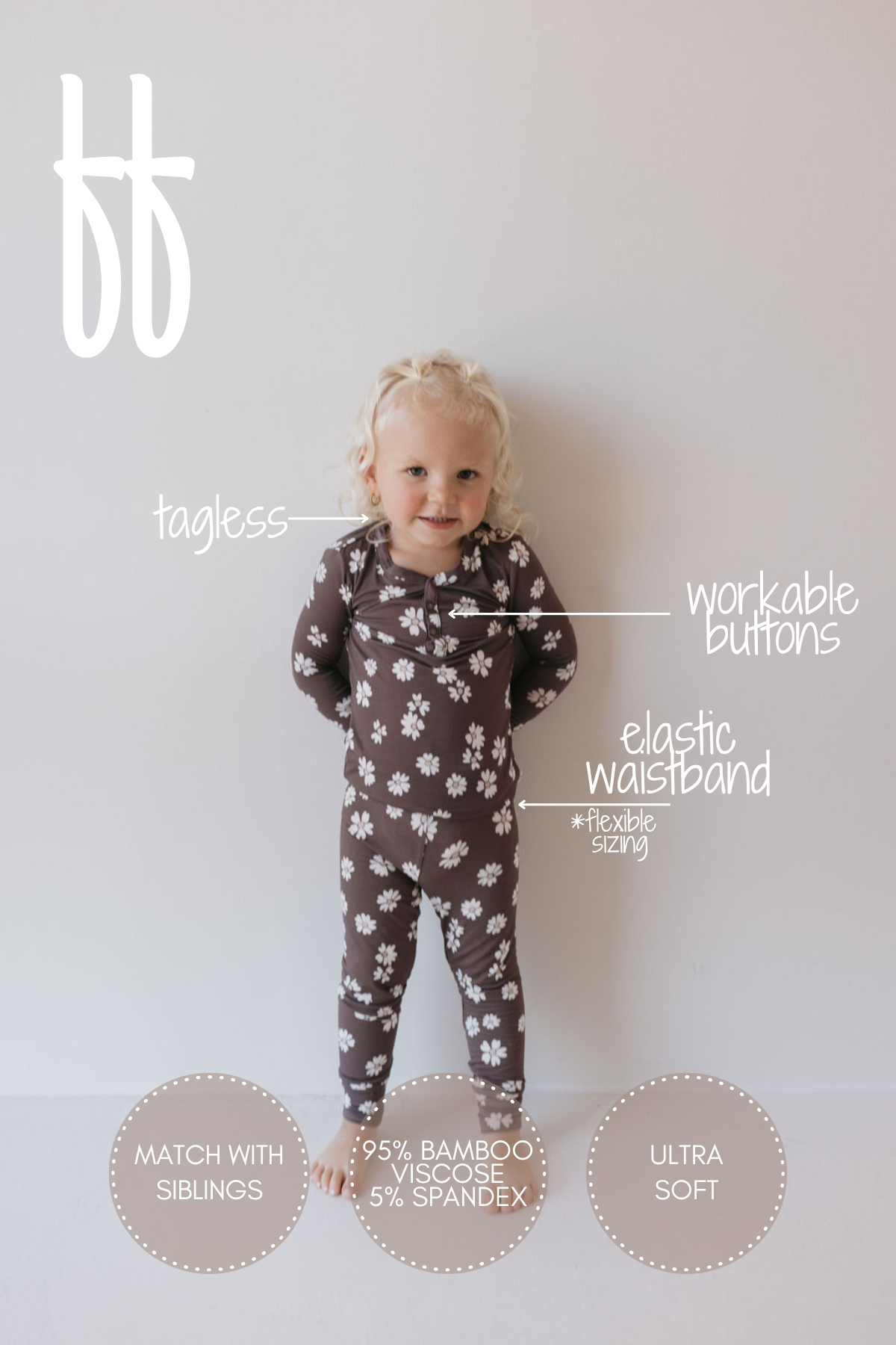 A toddler with blond hair stands against a light background wearing the "Midnight Meadow" two-piece pajamas from forever french baby, featuring a brown onesie embellished with white flower patterns. These hypoallergenic pajamas boast workable buttons, a tagless design, and an elastic waistband, crafted from 95% breathable bamboo clothing and 5% spandex.