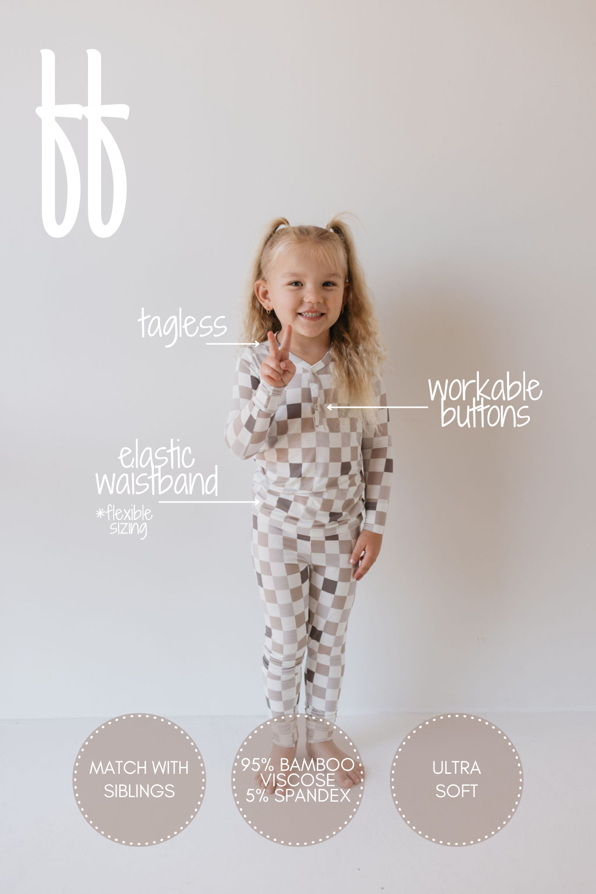 A young child with long, curly hair stands smiling in checkered pajamas. These breathable pajamas from "forever french baby," known as the Bamboo Two Piece Pajamas | Into the Woods Checkerboard, feature an elastic waistband, a tagless design, and workable buttons. They are crafted from 95% bamboo viscose and 5% spandex. The text highlights matching outfits for siblings and emphasizes the ultra-soft, hypoallergenic fabric.