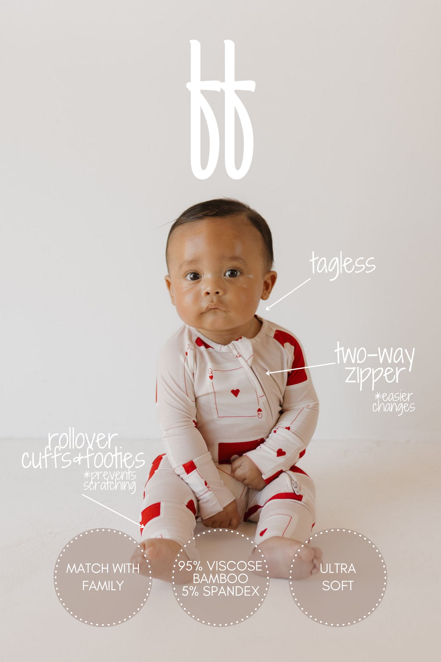 A baby in forever french baby's cream-colored Bamboo Zip Pajamas | Love Day, adorned with red hearts, sits against a white backdrop. These hypoallergenic pajamas feature a two-way zipper, rollover cuffs, are tagless, and made of 95% viscose from bamboo and 5% spandex.