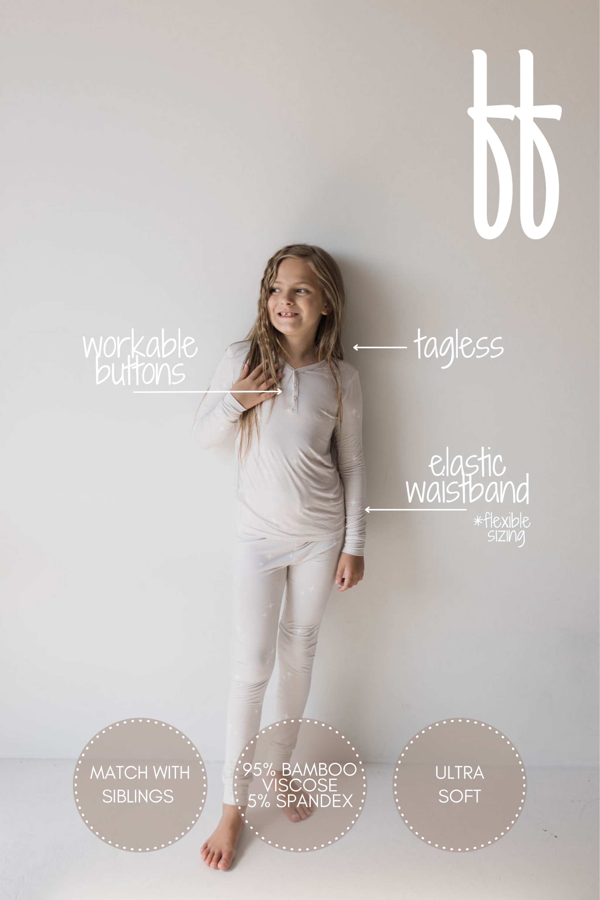 A young girl with long hair stands against a plain white background, wearing light-colored Bamboo Two Piece Pajamas | Sparkle! | ff club from Forever French Baby. She is looking off to the side and smiling. Text highlights features of the clothing, such as "workable buttons," "elastic waistband," "ultra soft," and "hypo-allergenic.