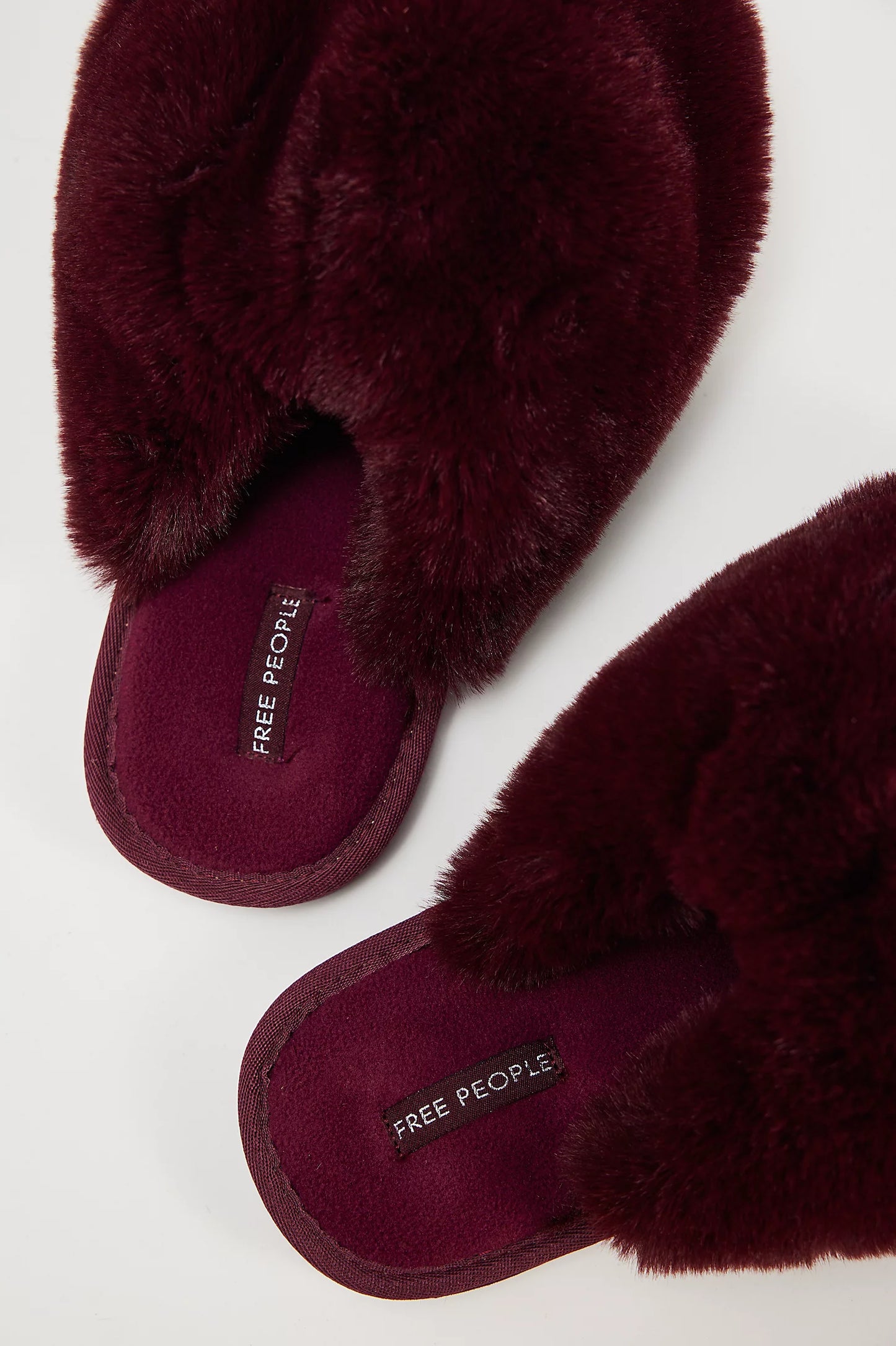 The Snowball Slipper by Free People features burgundy faux fur in a crisscross design with branded insoles, shown against a white background.
