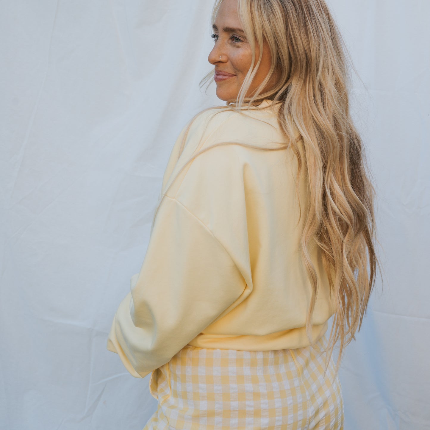 A woman with long blonde hair smiles over her shoulder in a forever french baby Adult Sweatshirt | ff Yellow against a white background—perfect for relaxed, everyday wear.