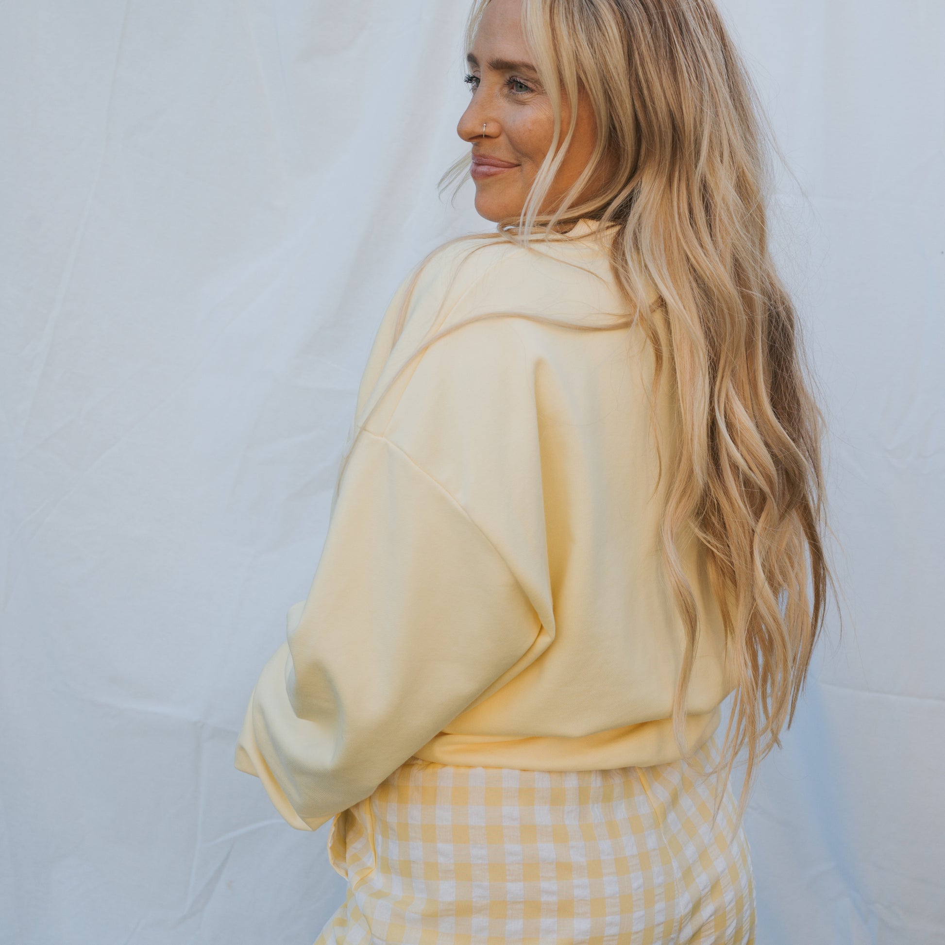 A woman with long blonde hair smiles over her shoulder in a forever french baby Adult Sweatshirt | ff Yellow against a white background—perfect for relaxed, everyday wear.