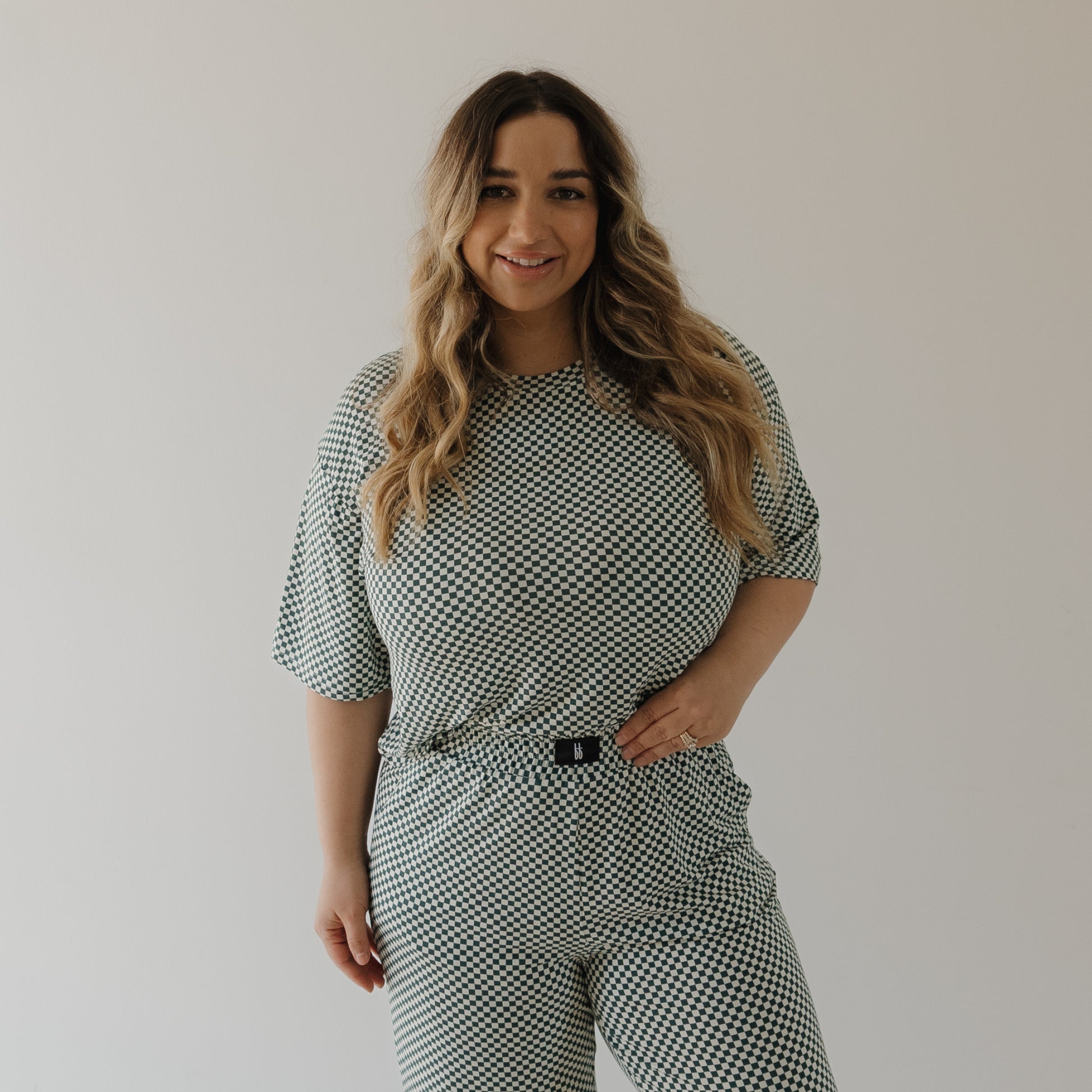 A woman with long wavy hair, smiling at the camera, models the forever french baby Women's Boxy Tee Lounge Set in Lucky Micro Check against a plain light background.