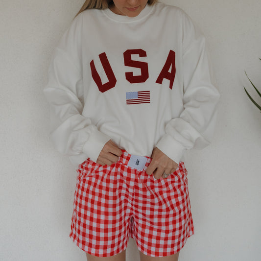 A person in a white "USA" sweatshirt and forever french baby Women's Boxer Shorts | Scarlet Gingham stands against a light background, their face partially out of view.