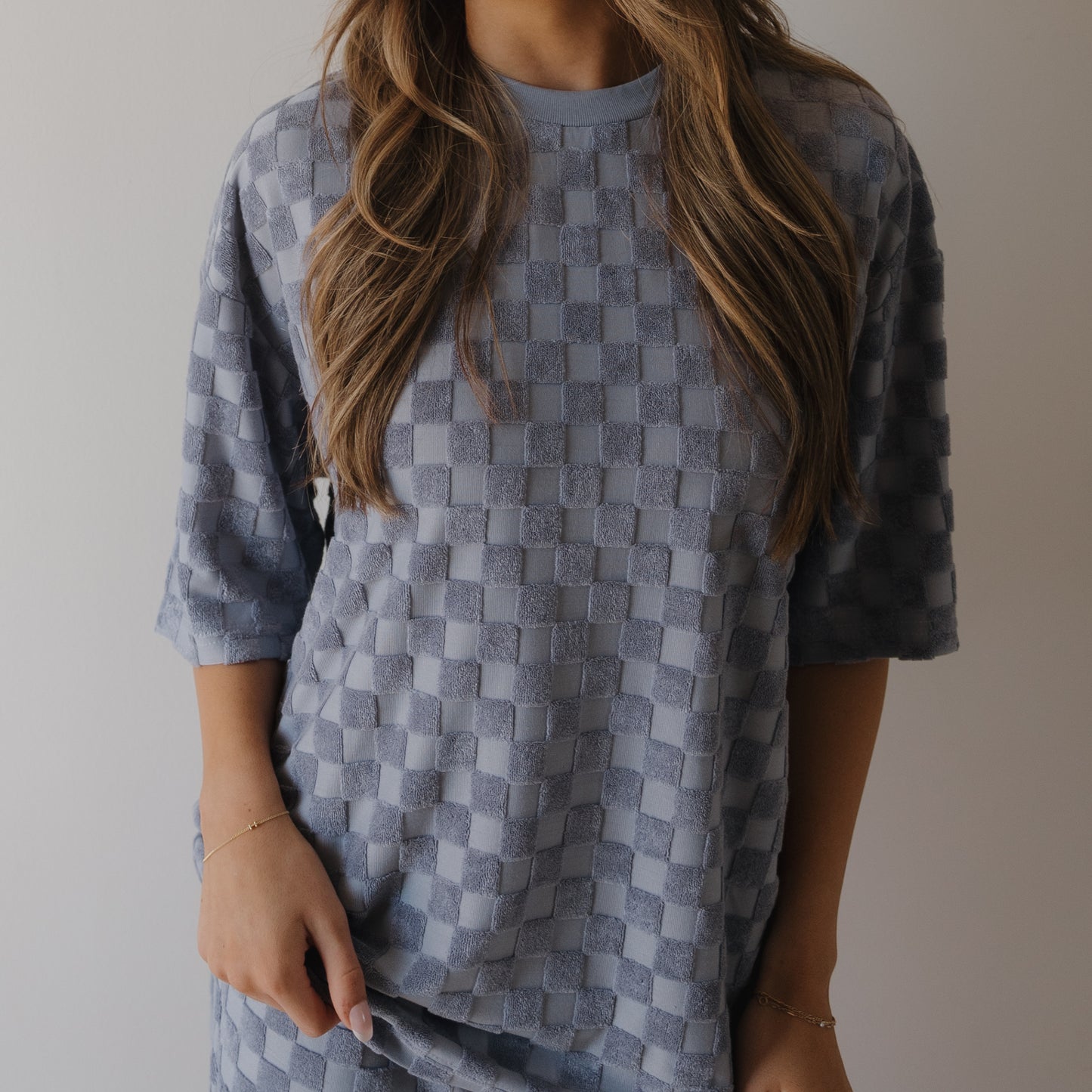 A woman models the forever french baby Women's Terry Short Set in Tradewinds, featuring a loose fit and short sleeves with a blue checkerboard texture. Her face is hidden, and her wavy light brown hair frames her against a plain background.