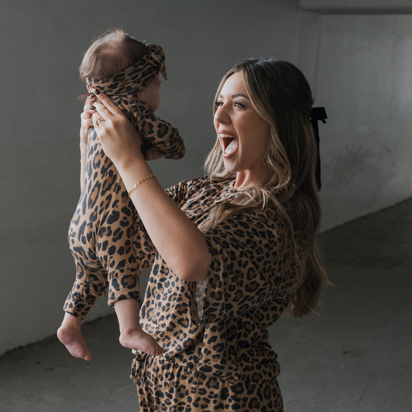 A woman joyfully lifts a baby indoors as both wear matching leopard print pajamas, with her in the forever french baby Women's Bamboo Short Set | Leopard.
