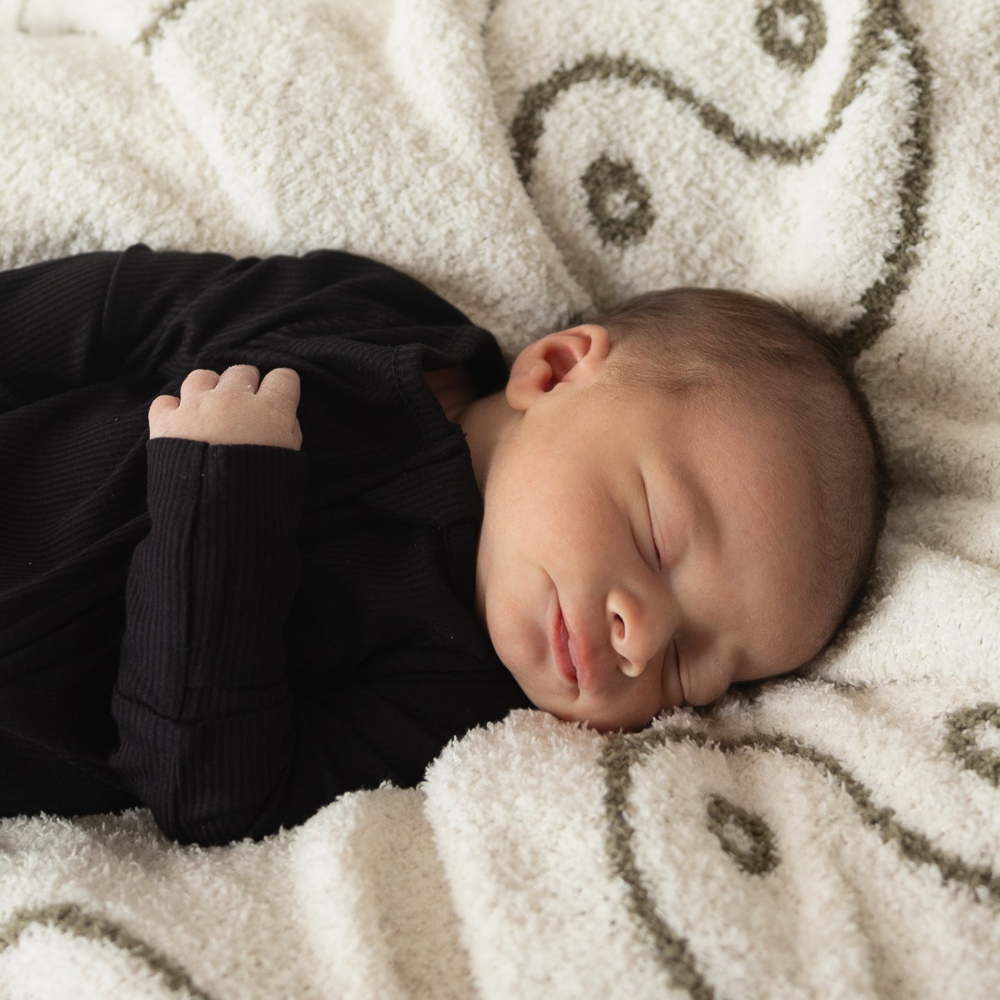 A newborn sleeps peacefully on a soft, white blanket, dressed in forever french baby Bamboo Zip Pajamas | Ribbed Black—breathable sleepwear that ensures comfort all night.