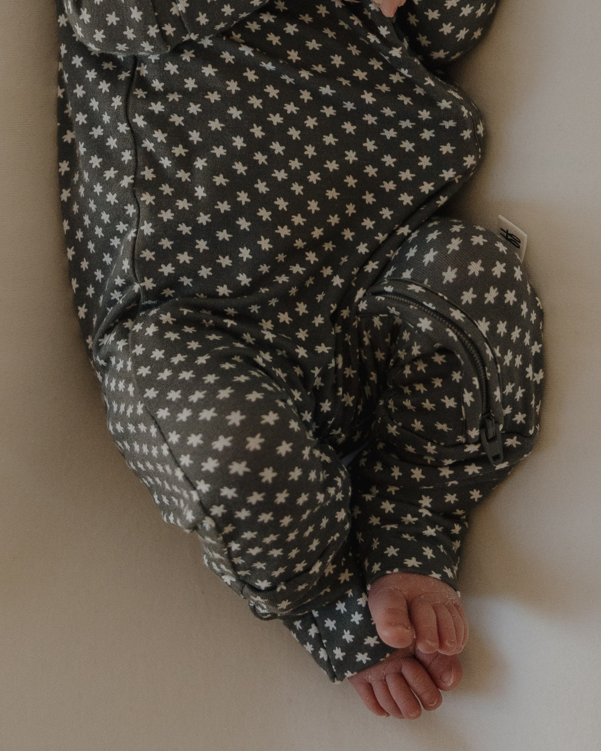 A baby wearing forever french baby Bamboo Zip Pajamas in the Green Flowers print lies on a light surface, showing bare feet and the zipper on this hypoallergenic outfit.
