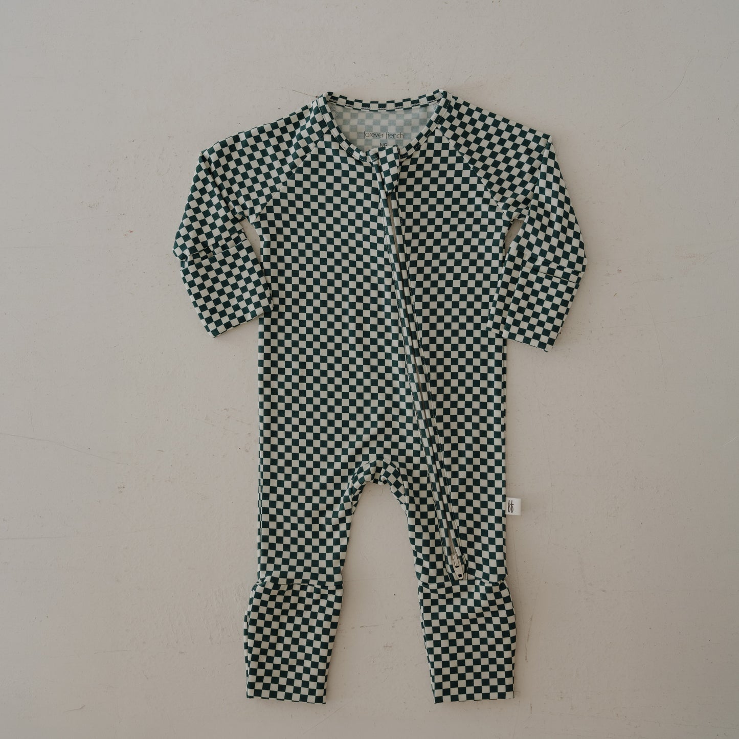 The forever french baby Bamboo Zip Pajamas | Lucky Micro Check are long-sleeve baby rompers with a black and white checkered pattern, crafted from breathable fabric with a front zipper closure, shown flat on a light-colored surface.