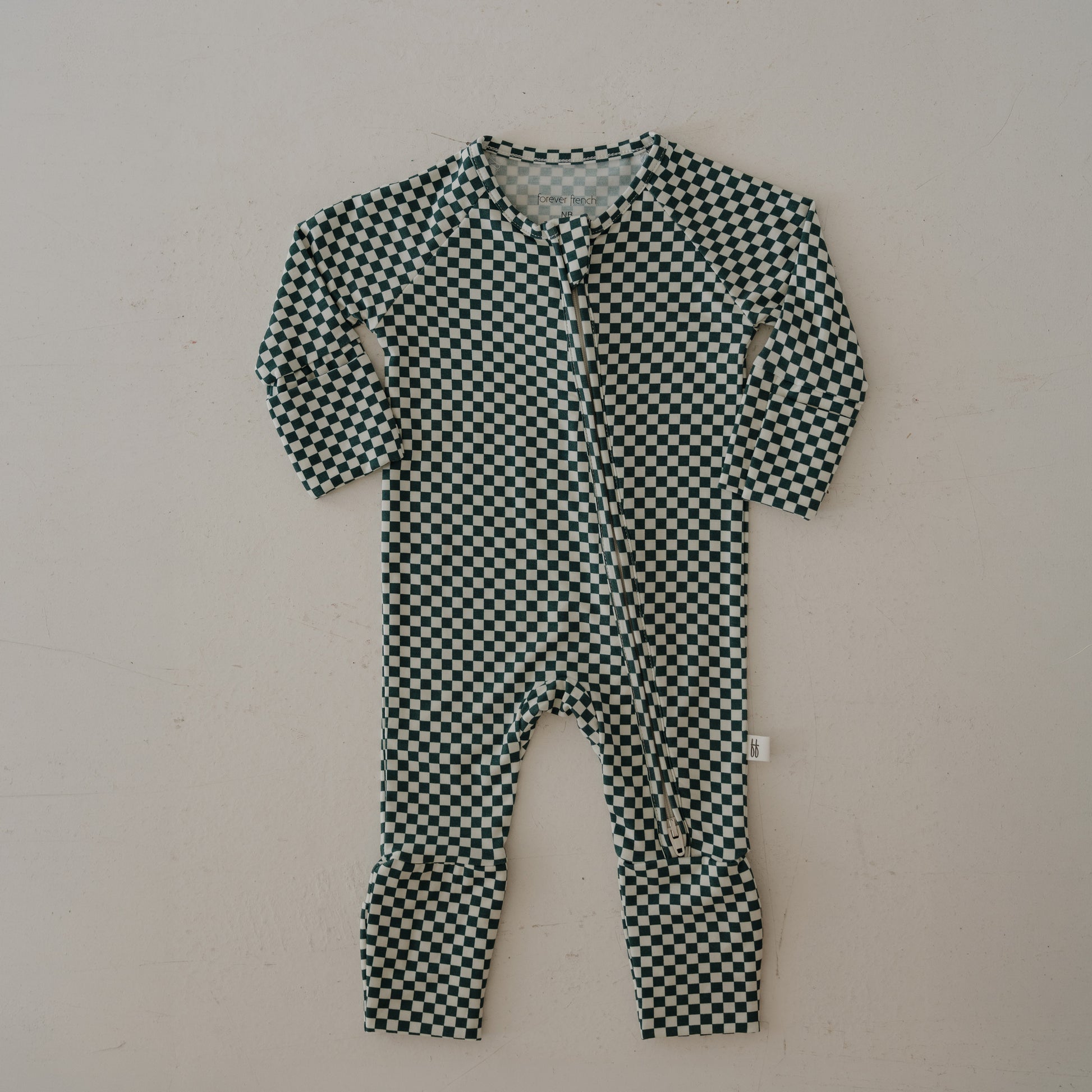 The forever french baby Bamboo Zip Pajamas | Lucky Micro Check are long-sleeve baby rompers with a black and white checkered pattern, crafted from breathable fabric with a front zipper closure, shown flat on a light-colored surface.