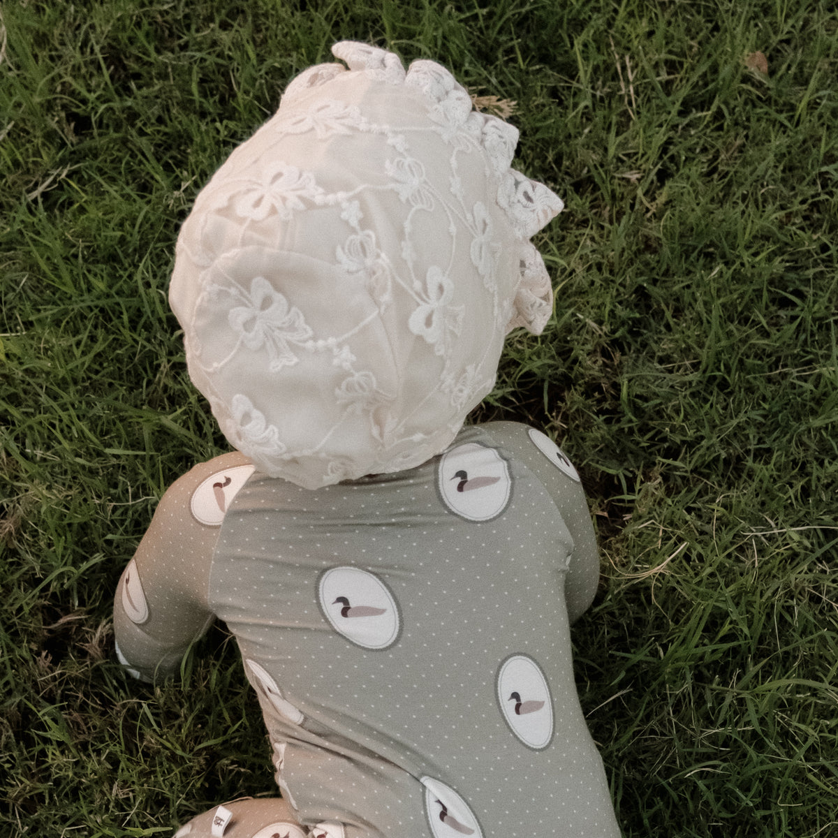 A baby wearing forever french baby’s Bamboo Zip Pajamas in the Mallard Frames print, crafted from hypoallergenic fabric, crawls on green grass, photographed from above.