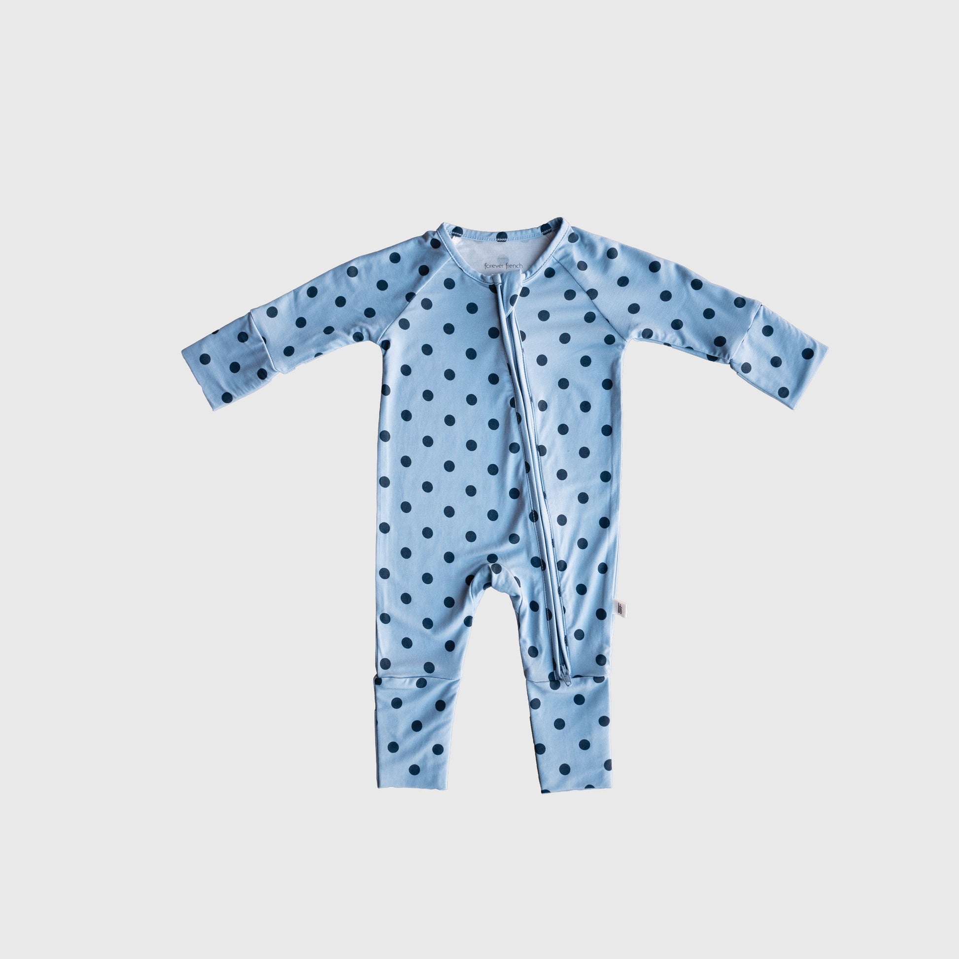 Dress your little one in the forever french baby Bamboo Zip Pajamas | Sully, featuring a light blue design with long sleeves and legs, accented by evenly spaced dark blue polka dots and a convenient diagonal zipper from neck to leg. Made from breathable baby sleepwear fabric, these pajamas provide cozy warmth and maximum comfort.