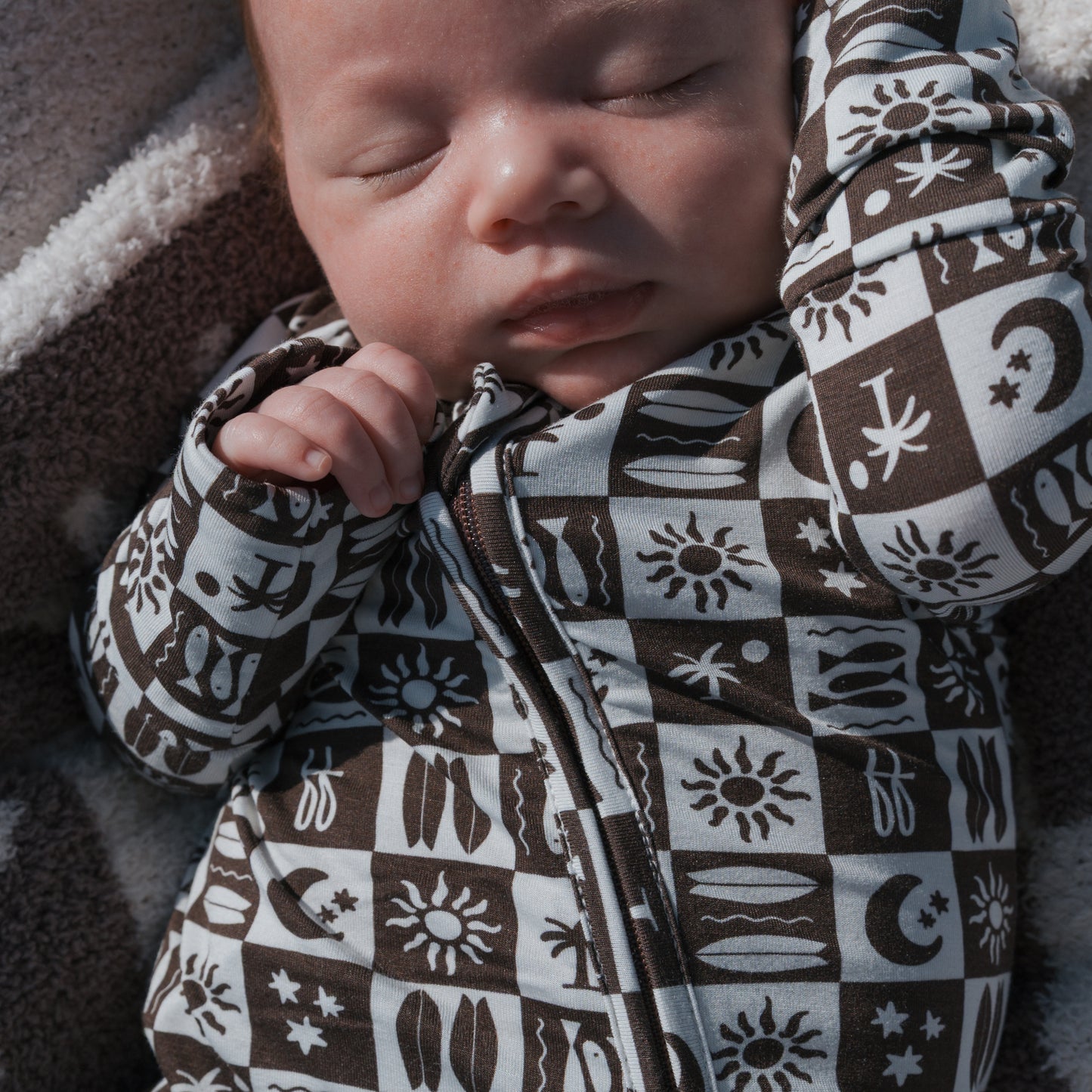 A sleeping baby wearing forever french baby's Bamboo Zip Pajamas | Summer Check—breathable, hypoallergenic zippered onesie—rests peacefully on a soft, fuzzy blanket.